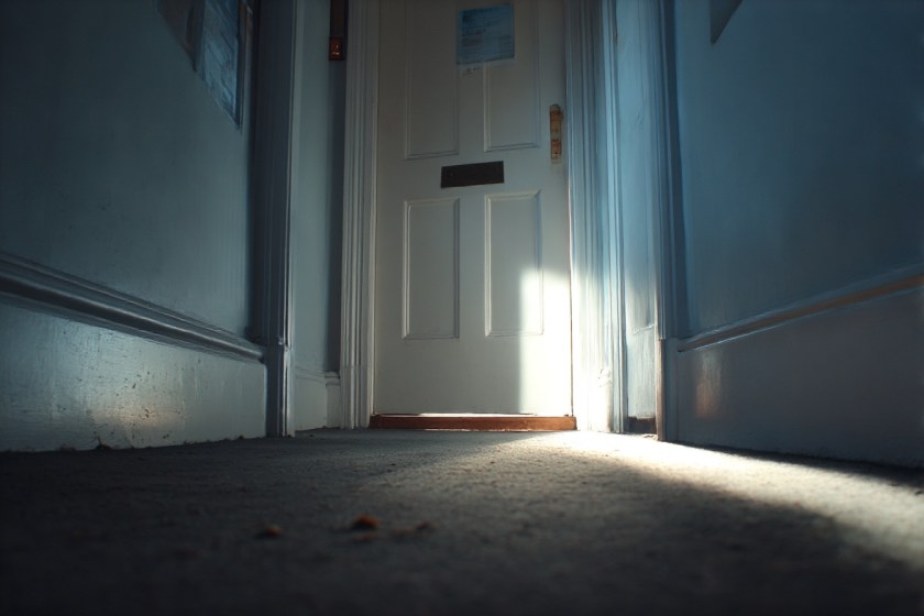 A corridor shot where the doorframe is central but the door itself is only partly visible. Light falling across the floor.