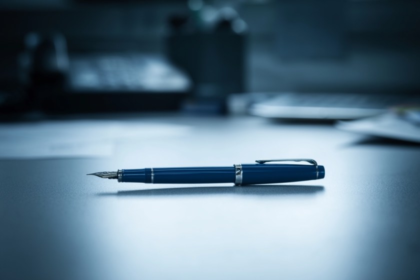 A single blue fountain pen lying on a grey government office desk. Harsh fluorescent lighting. The pen is perfectly centred. Everything else on the desk is slightly blurred. Hyper realistic. Cold colour palette.